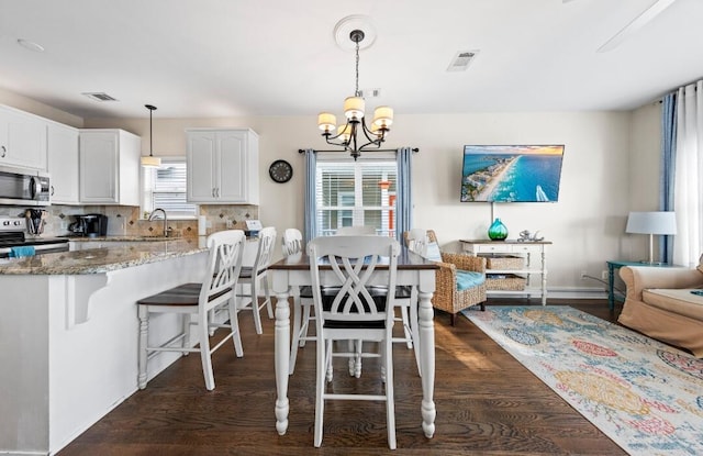 dining area featuring dark wood-style floors, visible vents, a notable chandelier, and baseboards