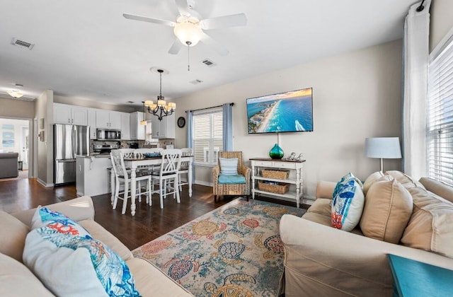 living area with ceiling fan with notable chandelier, visible vents, baseboards, and dark wood-type flooring