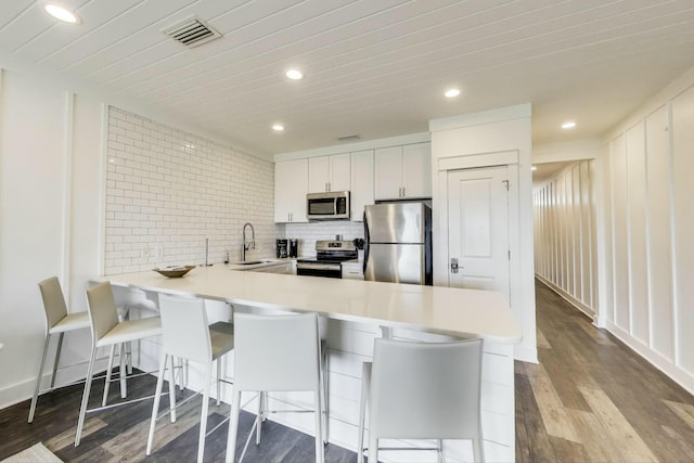 kitchen with dark wood-type flooring, backsplash, visible vents, a peninsula, and appliances with stainless steel finishes