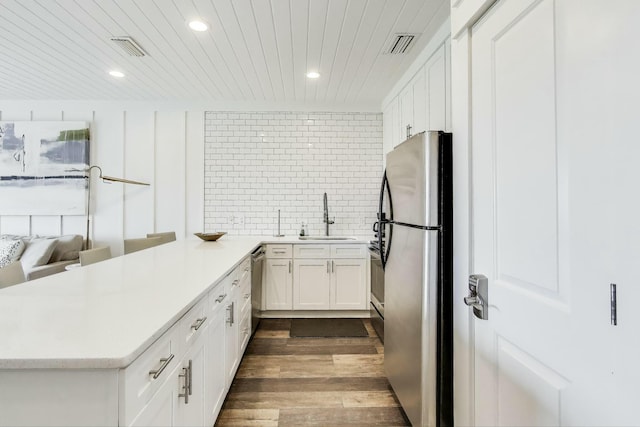 kitchen with decorative backsplash, a peninsula, stainless steel appliances, dark wood finished floors, and a sink