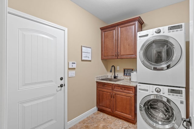 laundry room featuring stacked washer / dryer, light tile patterned floors, cabinet space, a sink, and baseboards