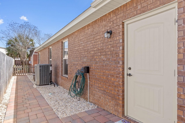 entrance to property featuring brick siding, fence, and central AC unit