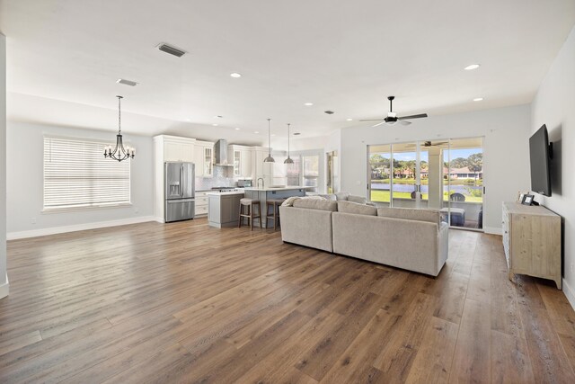 living area with ceiling fan with notable chandelier, visible vents, recessed lighting, wood finished floors, and baseboards