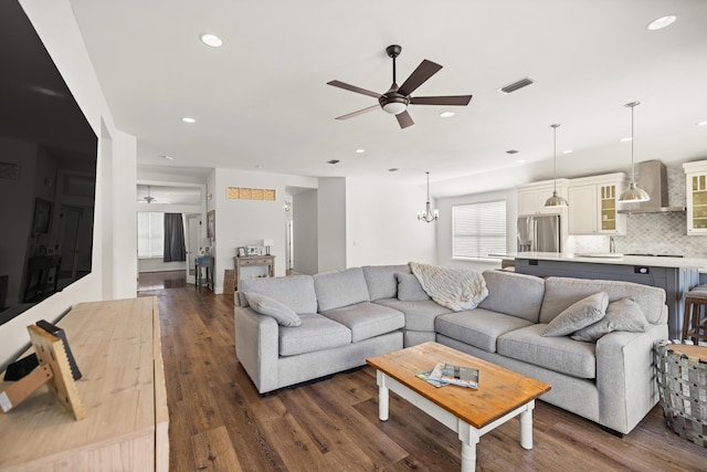 living room featuring visible vents, ceiling fan with notable chandelier, and dark wood finished floors