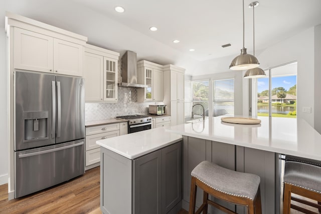 kitchen with wall chimney range hood, a breakfast bar, appliances with stainless steel finishes, wood finished floors, and backsplash
