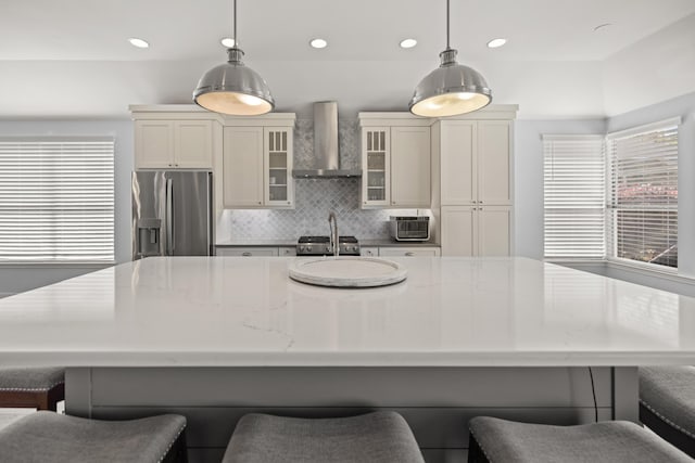 kitchen featuring tasteful backsplash, wall chimney range hood, stainless steel fridge, hanging light fixtures, and a spacious island