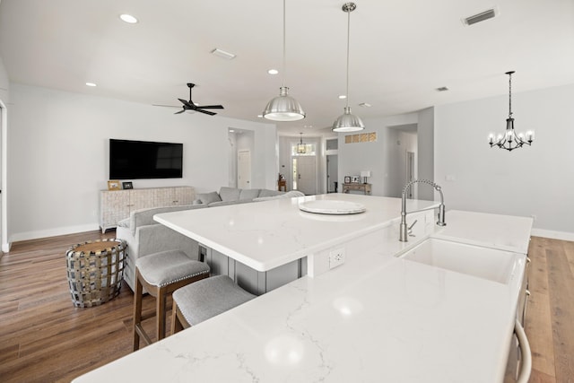 kitchen featuring visible vents, a sink, recessed lighting, wood finished floors, and light stone counters