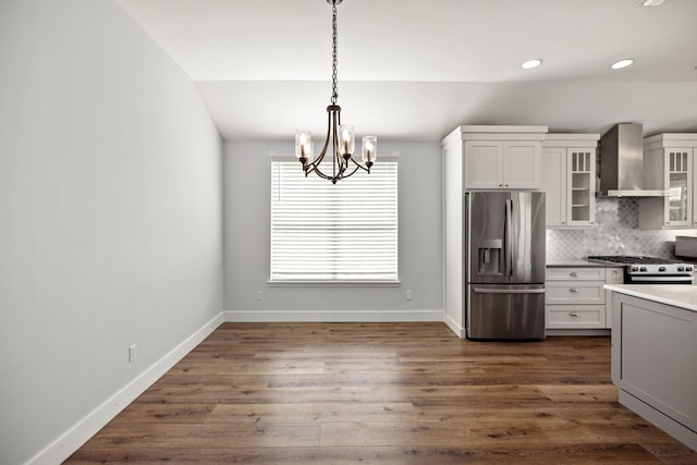 kitchen with an inviting chandelier, wall chimney exhaust hood, appliances with stainless steel finishes, dark wood-type flooring, and decorative backsplash