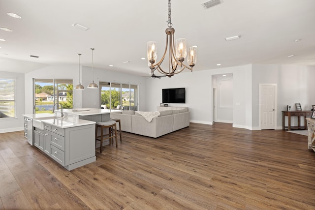 kitchen with visible vents, open floor plan, light countertops, an island with sink, and wood finished floors