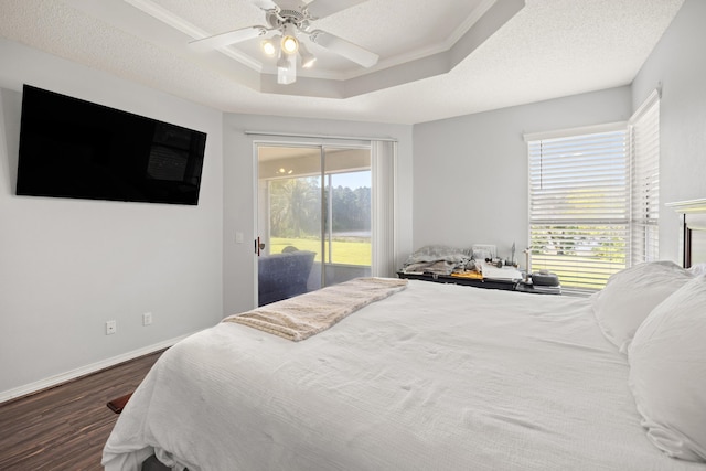 bedroom with a tray ceiling, access to outside, dark wood-style flooring, and multiple windows