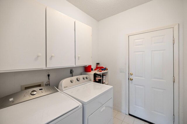 laundry area with a textured ceiling, washing machine and clothes dryer, cabinet space, and light tile patterned floors