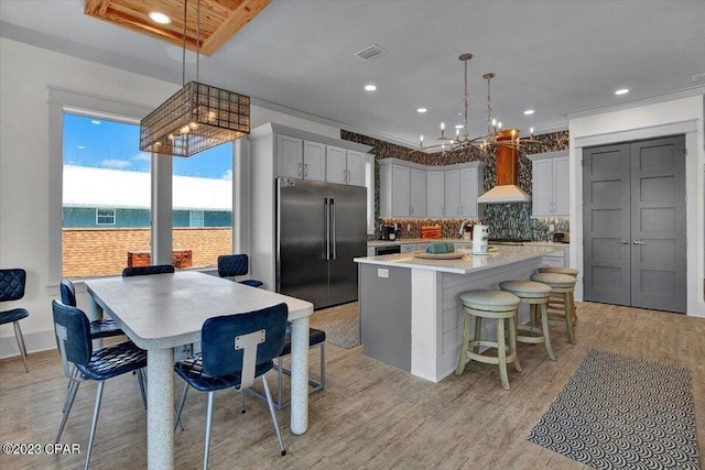 8320 Surf Dr, Panama City Beach, FL 32408 - kitchen with a center island with sink, decorative backsplash, wall chimney exhaust hood, high quality fridge, and light wood-type flooring