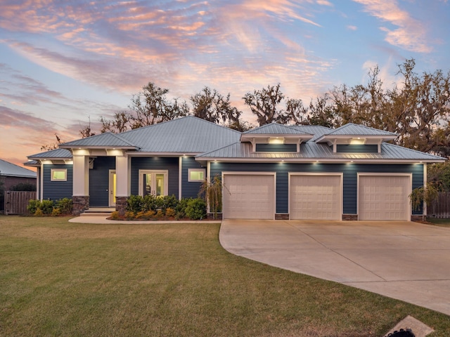 prairie-style home with concrete driveway, an attached garage, stone siding, metal roof, and a yard