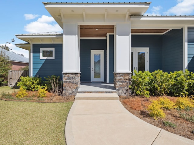 doorway to property with stone siding, metal roof, covered porch, and a yard