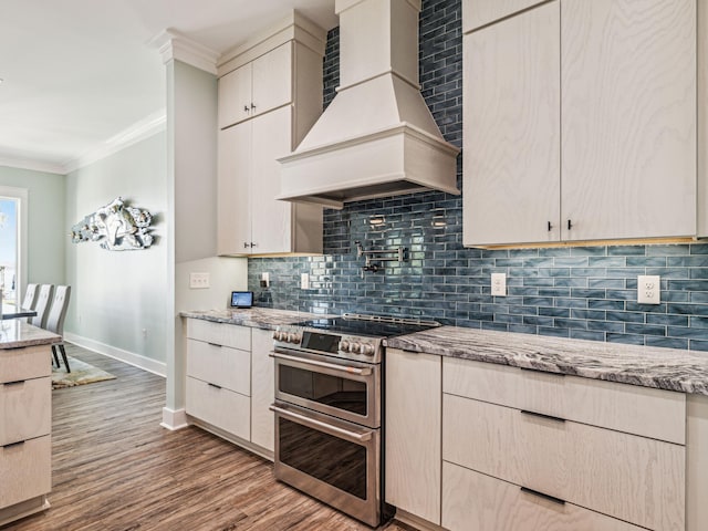 kitchen with ornamental molding, decorative backsplash, range with two ovens, light stone countertops, and wall chimney exhaust hood