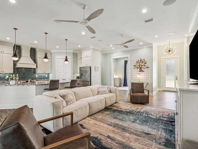 living room featuring ornamental molding, baseboards, visible vents, a ceiling fan, and wood finished floors