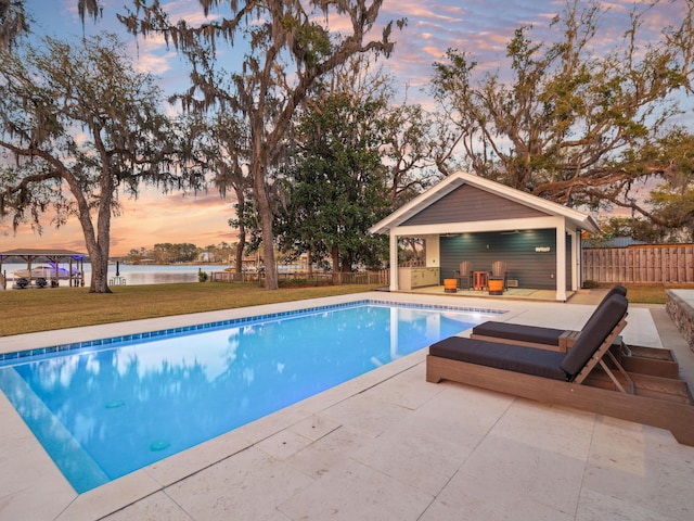 pool at dusk featuring an outdoor structure, fence, a patio, a fenced in pool, and a lawn