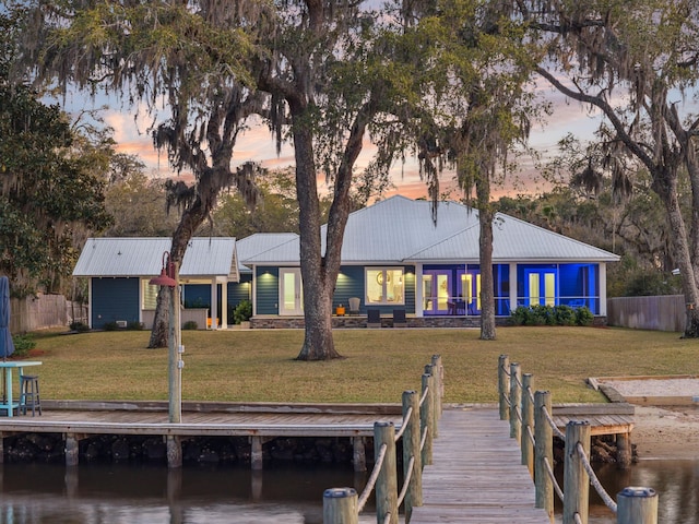 view of dock featuring a lawn, a water view, and fence