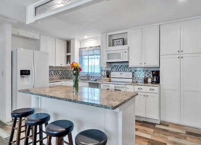 kitchen with white appliances, a breakfast bar, decorative backsplash, light wood-style floors, and white cabinetry