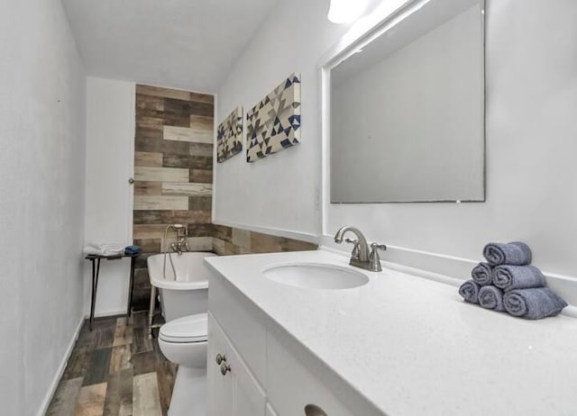 full bathroom featuring vanity, wooden walls, wood finished floors, a freestanding bath, and toilet