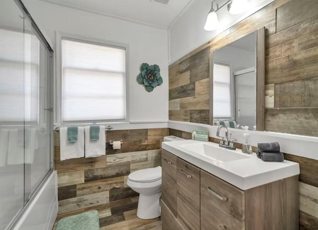 full bathroom with a wainscoted wall, toilet, wood finished floors, shower / bath combination with glass door, and vanity