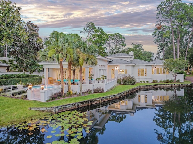rear view of property featuring a water view, fence, a chimney, a fenced in pool, and a lawn
