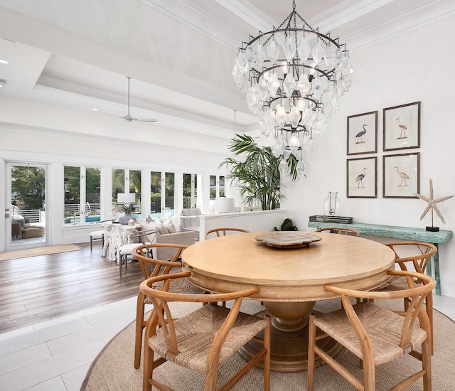 dining area with an inviting chandelier, a raised ceiling, ornamental molding, and light wood-style floors
