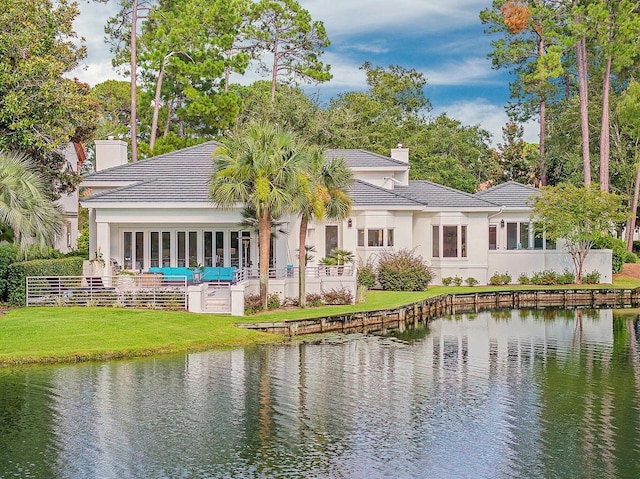 rear view of property with a water view, a tiled roof, a chimney, stucco siding, and a lawn