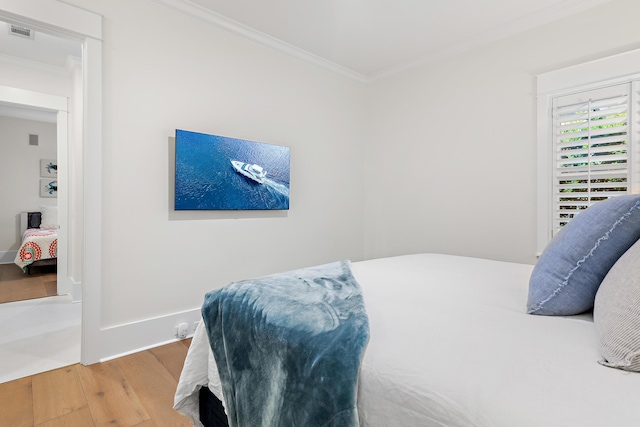 bedroom featuring baseboards, visible vents, crown molding, and wood finished floors