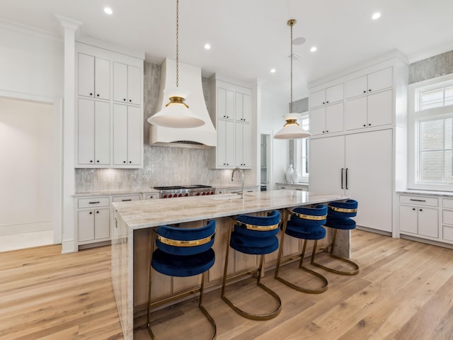 267 Tyler Dr, Santa Rosa Beach, FL 32459 - kitchen with custom range hood, light wood-type flooring, a kitchen island with sink, and decorative backsplash