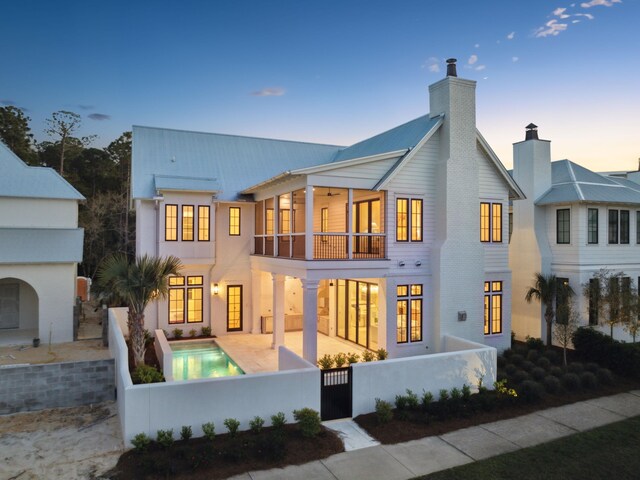 267 Tyler Dr, Santa Rosa Beach, FL 32459 - back of house at dusk featuring a chimney, a balcony, a fenced front yard, a gate, and a patio area