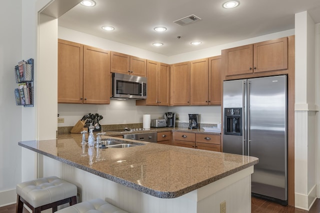 kitchen with visible vents, a peninsula, a kitchen bar, stainless steel appliances, and stone counters