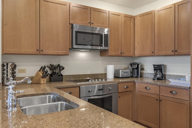 kitchen with brown cabinetry, a sink, appliances with stainless steel finishes, and light stone counters