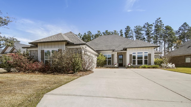 view of front of house featuring roof with shingles, an attached garage, board and batten siding, driveway, and a front yard