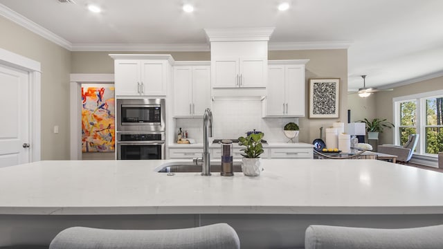 kitchen with ornamental molding, a center island with sink, tasteful backsplash, and appliances with stainless steel finishes