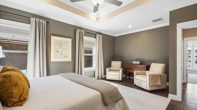 bedroom with visible vents, crown molding, baseboards, wood finished floors, and a raised ceiling