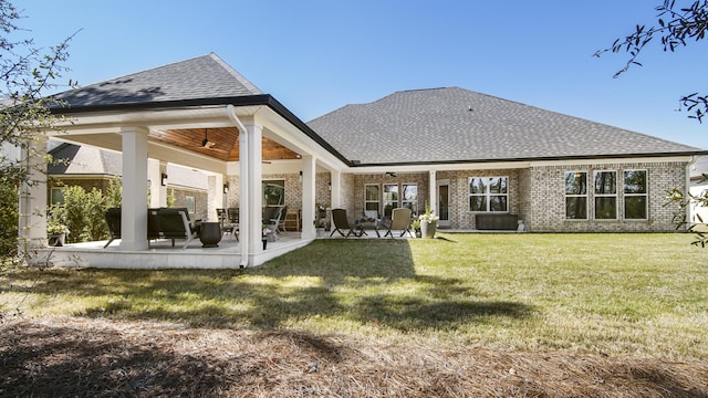 rear view of house with a ceiling fan, brick siding, a shingled roof, and a yard