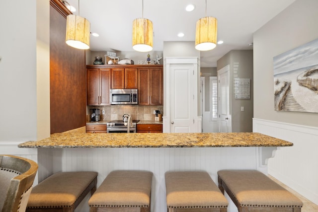 26 Classic Court Ln, Santa Rosa Beach, FL 32459 - kitchen with a peninsula, a wainscoted wall, decorative backsplash, pendant lighting, and appliances with stainless steel finishes