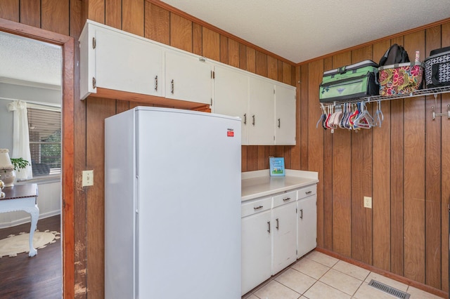 24776 Fifth Ave, Florala, AL 36442 - kitchen with visible vents, a textured ceiling, freestanding refrigerator, wood walls, and white cabinets