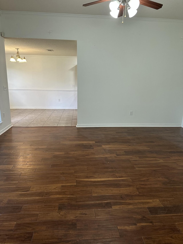empty room with ornamental molding, ceiling fan with notable chandelier, baseboards, and dark wood-type flooring