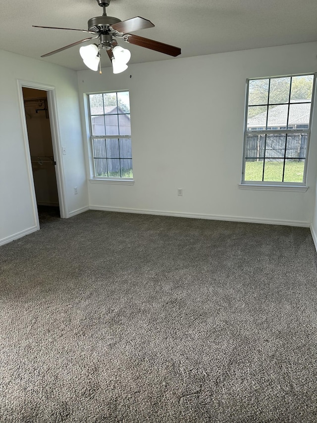 unfurnished room with baseboards, a ceiling fan, and dark colored carpet