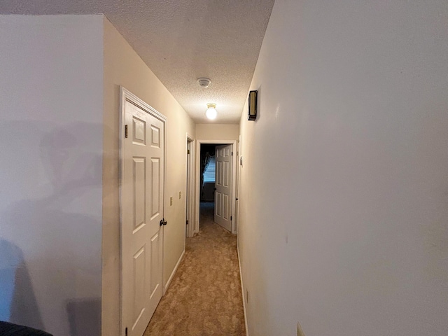 hall featuring baseboards, a textured ceiling, and light carpet