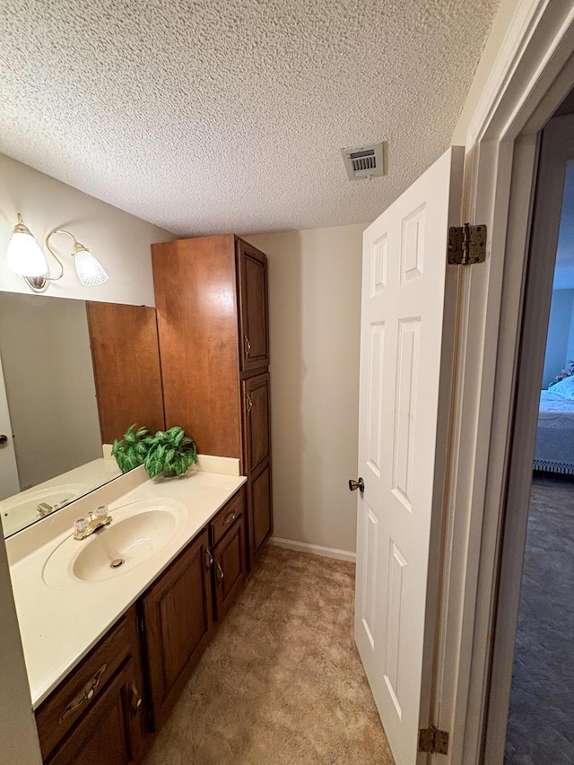 bathroom with ensuite bathroom, a textured ceiling, visible vents, baseboards, and vanity