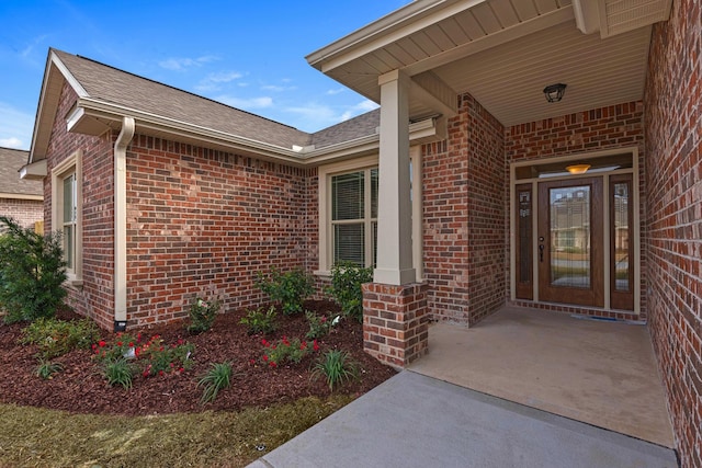 view of exterior entry with a shingled roof and brick siding