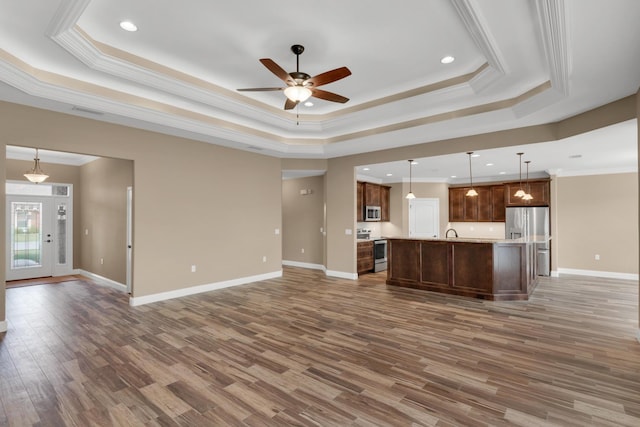 kitchen with wood finished floors, stainless steel appliances, a ceiling fan, open floor plan, and a tray ceiling