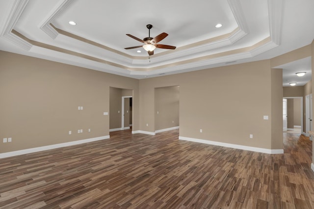 empty room featuring a tray ceiling, ceiling fan, and dark wood finished floors