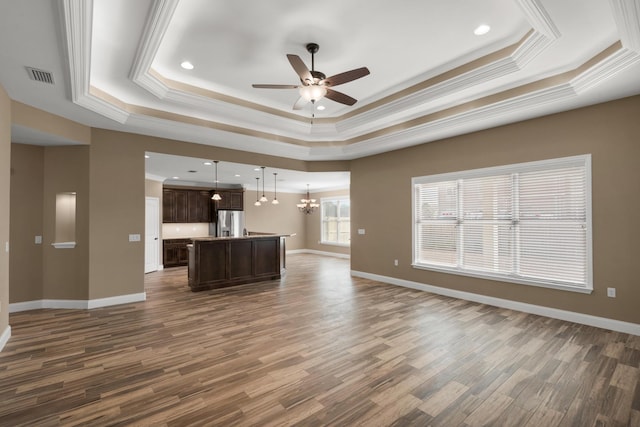 unfurnished living room with ceiling fan with notable chandelier, visible vents, dark wood-type flooring, and a raised ceiling