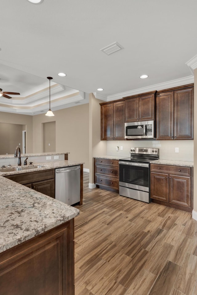kitchen with a tray ceiling, a sink, appliances with stainless steel finishes, light wood-type flooring, and visible vents