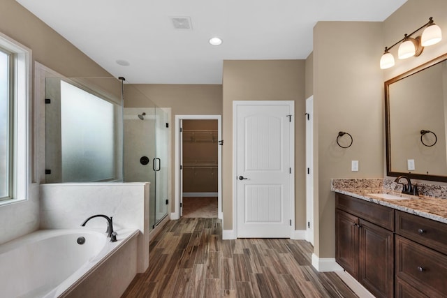 bathroom featuring a stall shower, vanity, a garden tub, wood finished floors, and a walk in closet