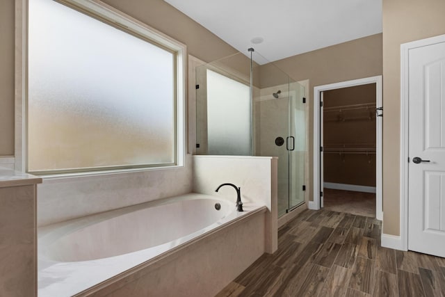 bathroom featuring a shower stall, wood finished floors, a spacious closet, and a garden tub